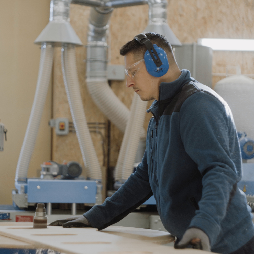 Osoba w rękawicach ochronnych obrabia drewnianą płytę